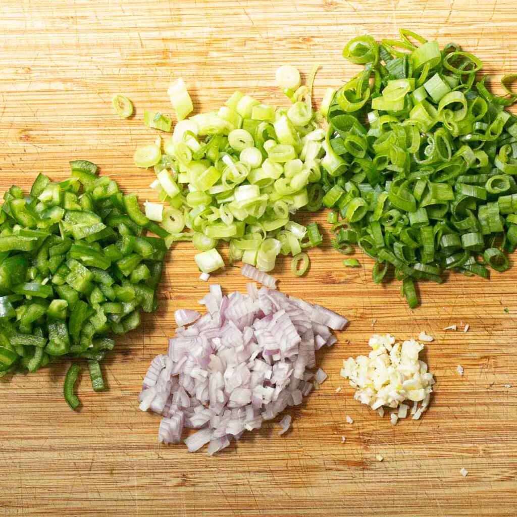 chopped scallions, peppers and onions on a wooden board