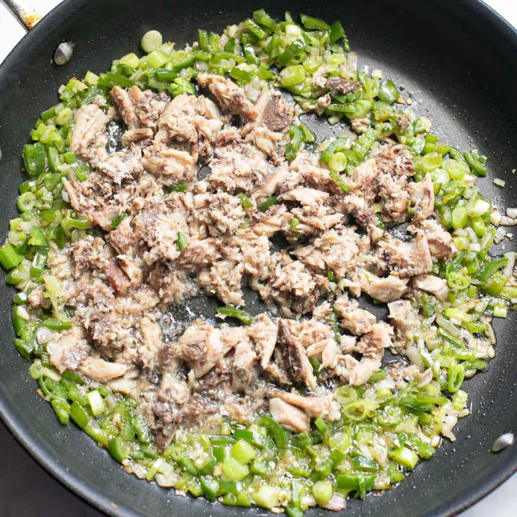 chopped scallions and peppers and sardines cooking in a pan