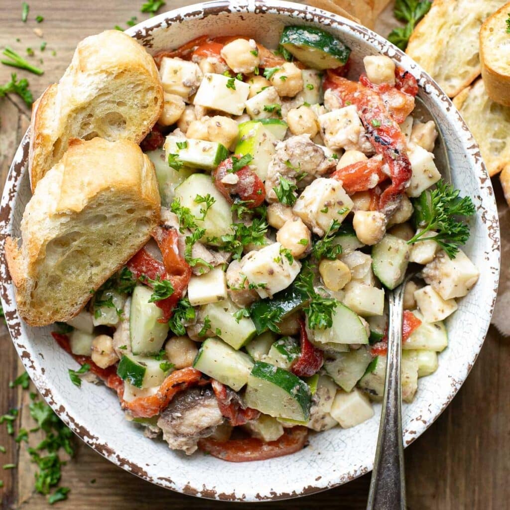 sardine salad in a white bowl with a silver serving spoon and baguette slices on the side