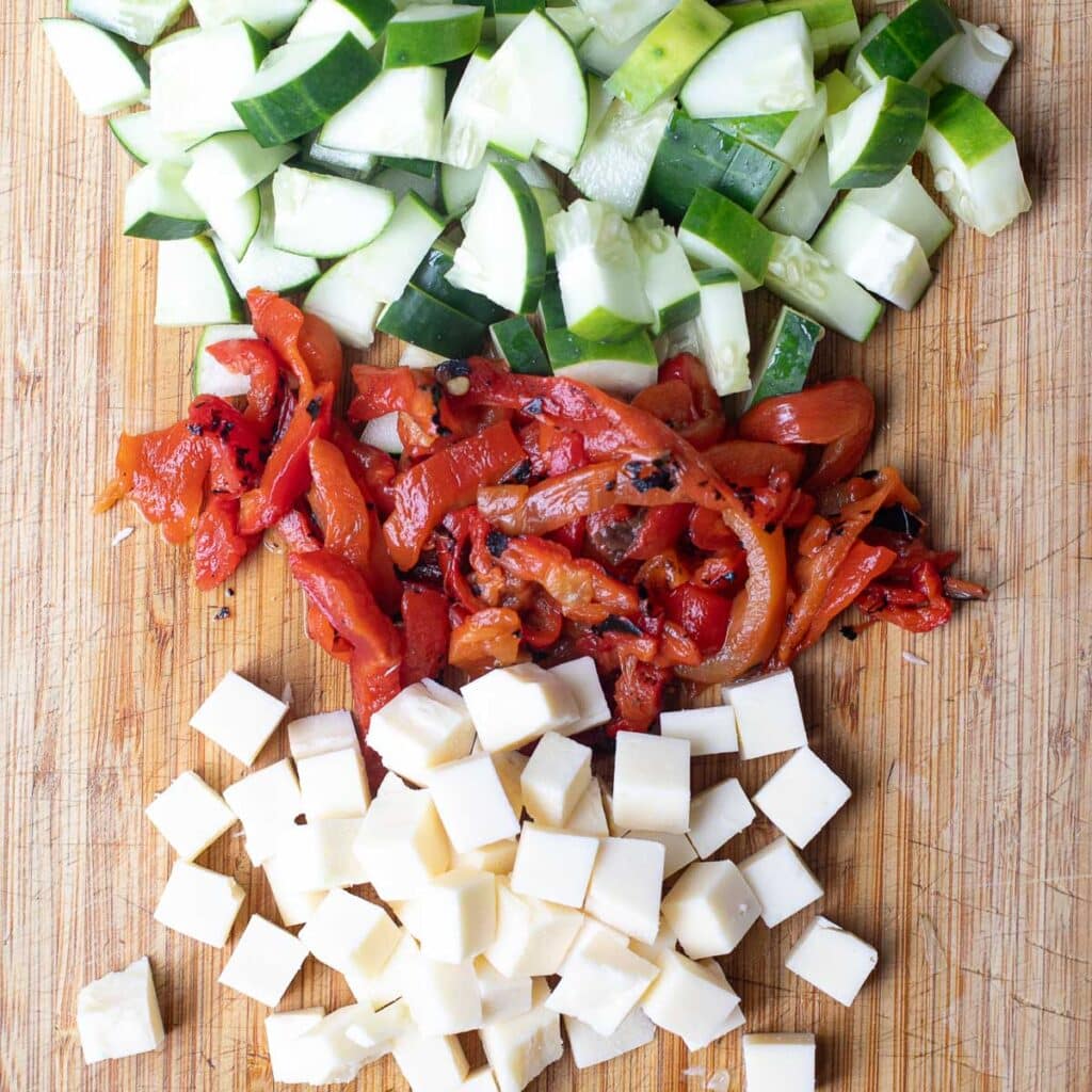 chopped tomatoes, roasted red peppers and cubed cheese on a wooden board