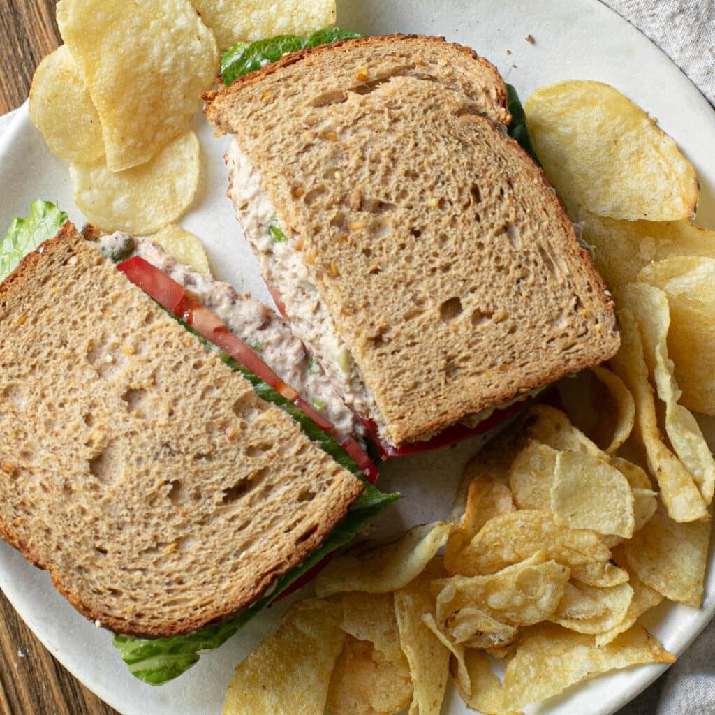 sardine sandwich on a white plate with potato chips