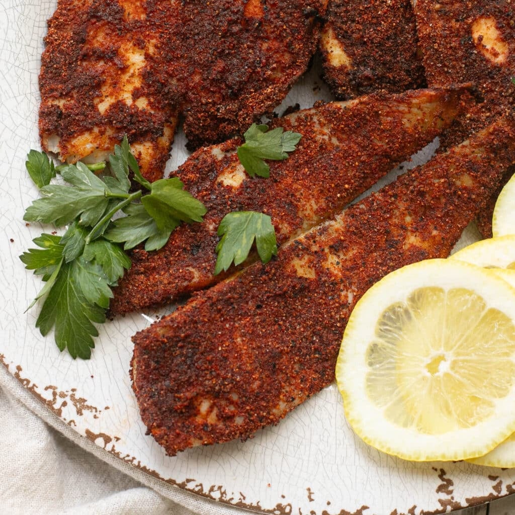air fryer tilapia on a white plate with lemon slices and fresh parsley