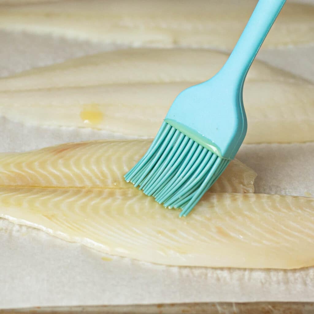 a fillet of tilapia being brushed with oil
