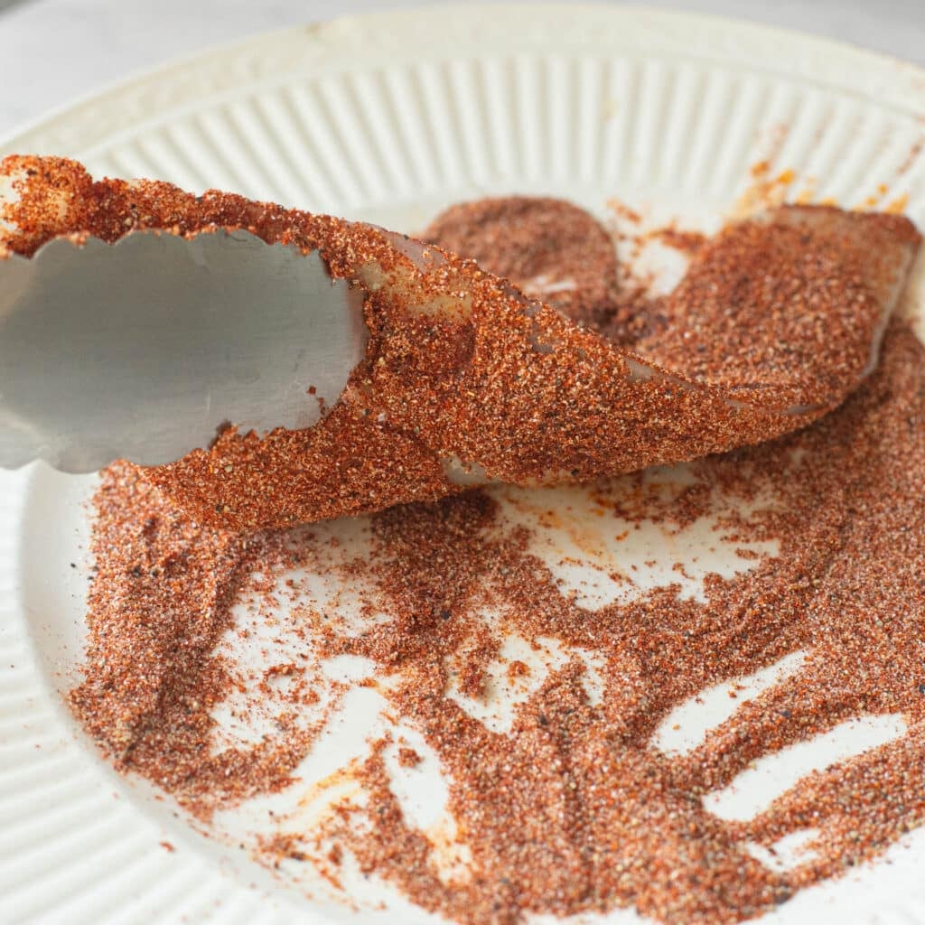 a fillet of tilapia being coated in a dry seasoning mix