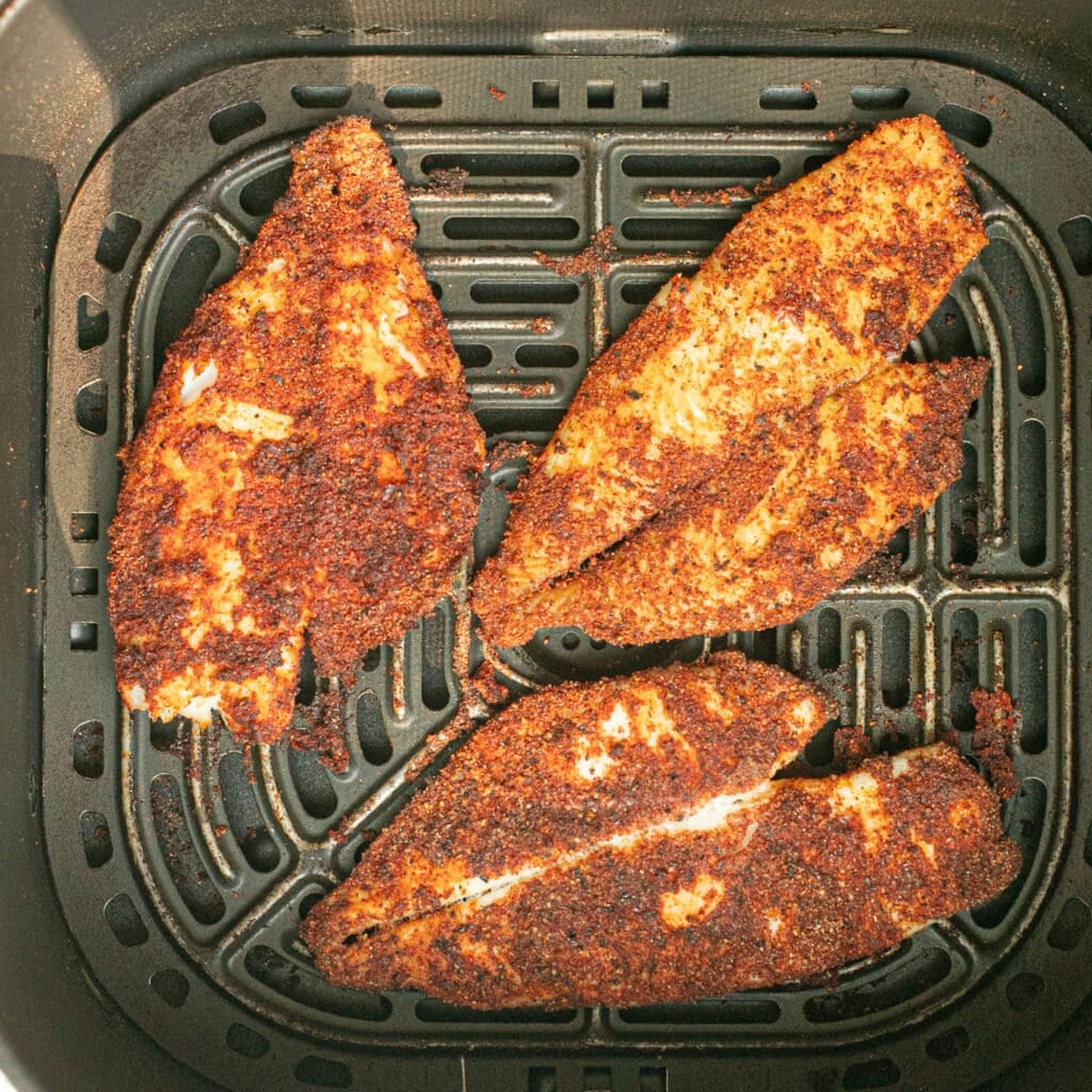 seasoned tilapia filets in the basket of an air fryer
