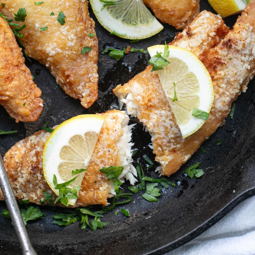fried tilapia fillet cut in half and topped with lemon slices