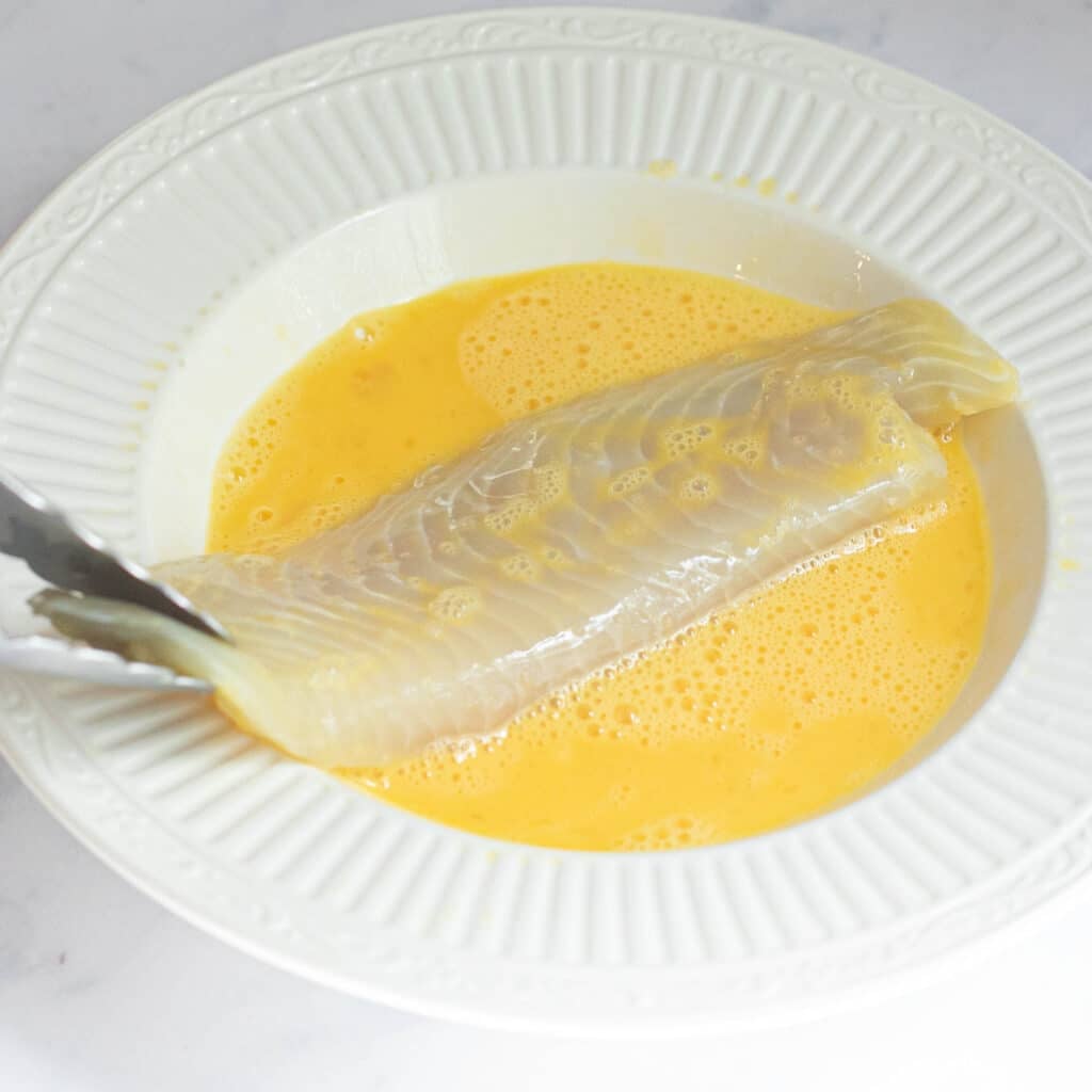 tilapia fillet being dredged in beaten egg