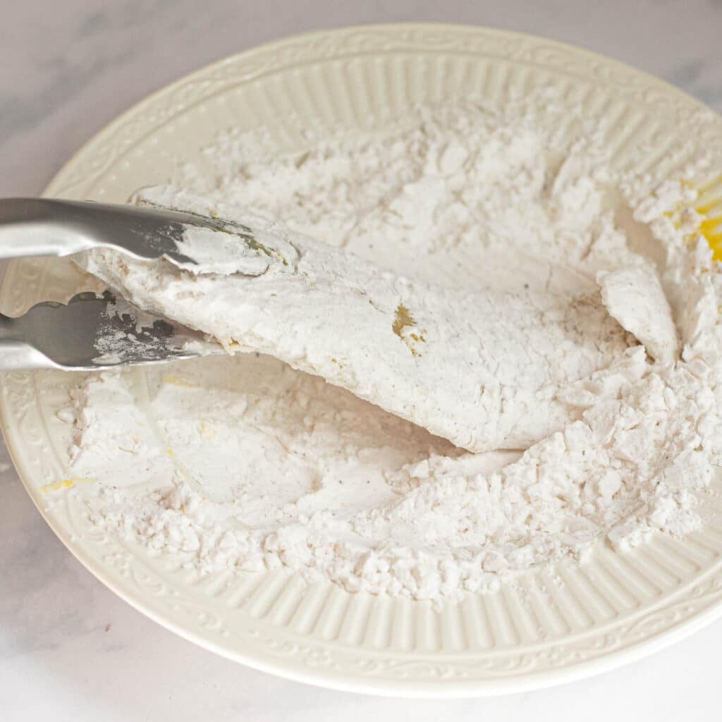 tilapia filet being dredged in cornstarch