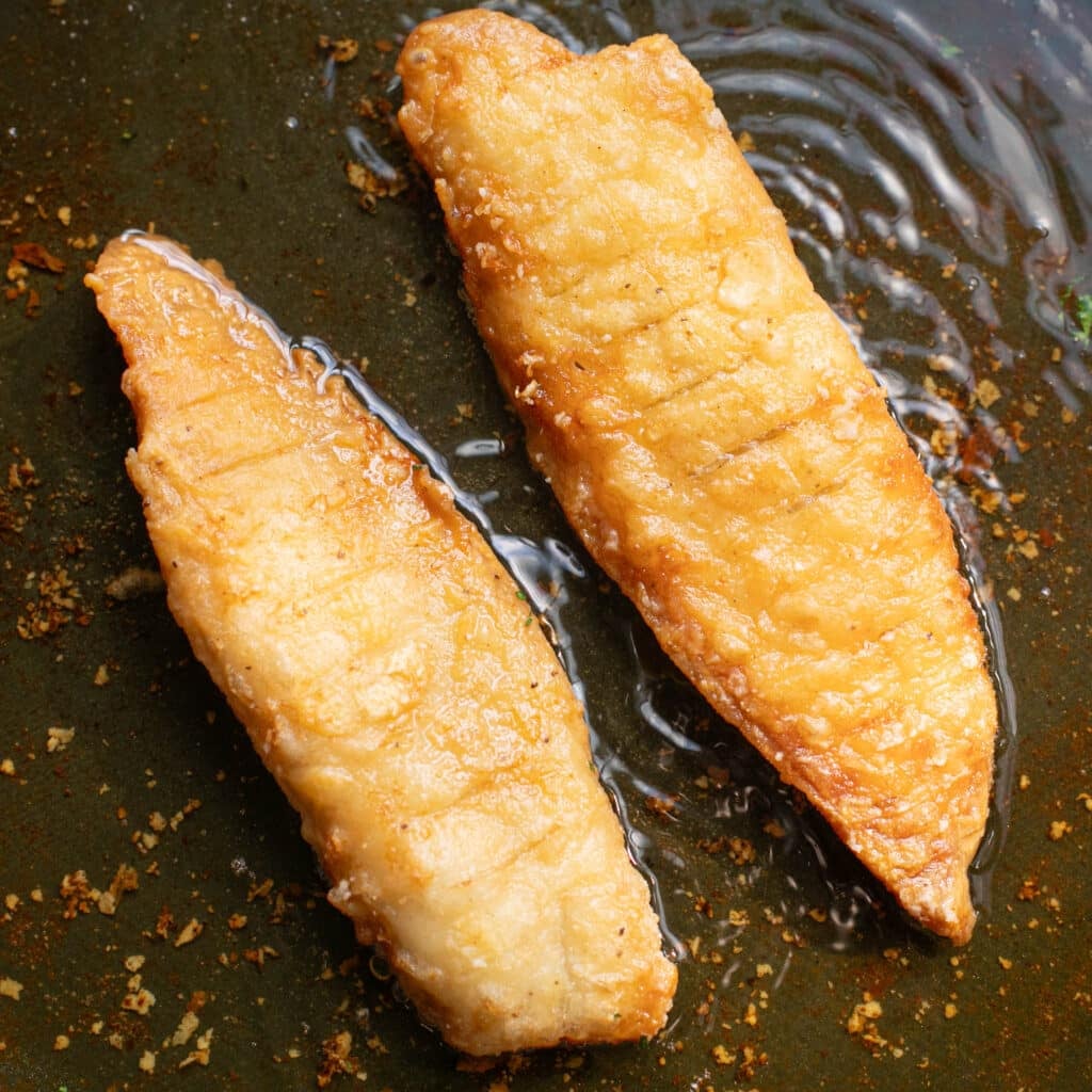 battered tilapia fillets frying in a cast iron pan
