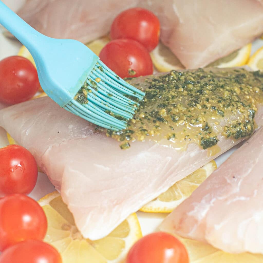 pesto sauce being brushed onto a fillet of snapper before baking