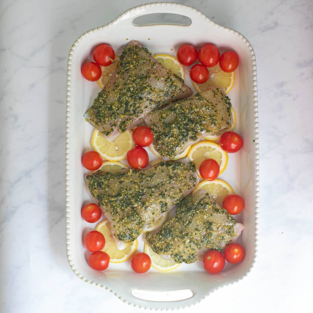 snapper fillets arranged in a baking dish with lemon slices and cherry tomatoes before baking