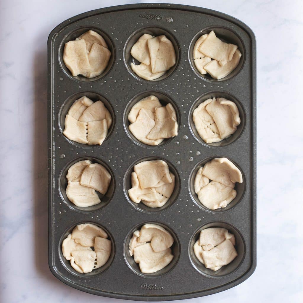 squares of crescent dough in a muffin tin