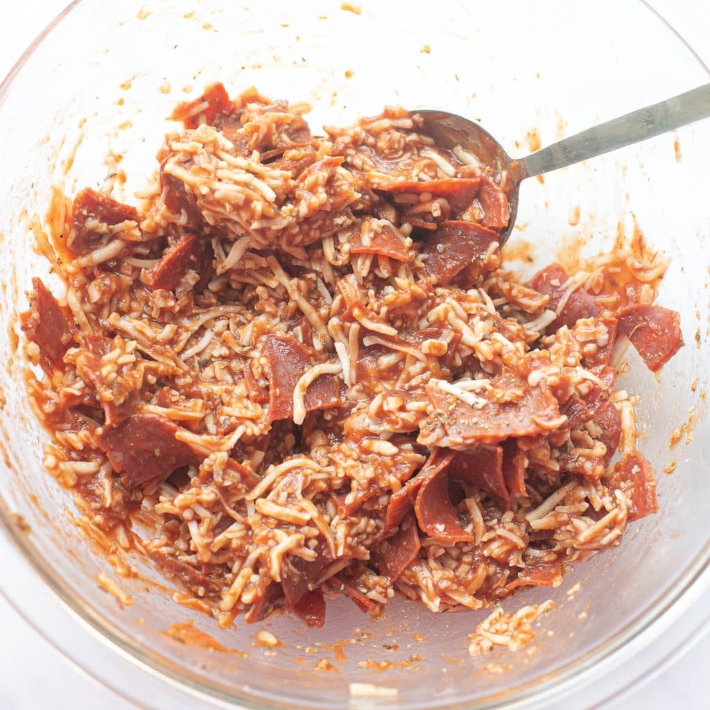 mozzarella cheese, pizza sauce and chopped pepperoni in a glass mixing bowl