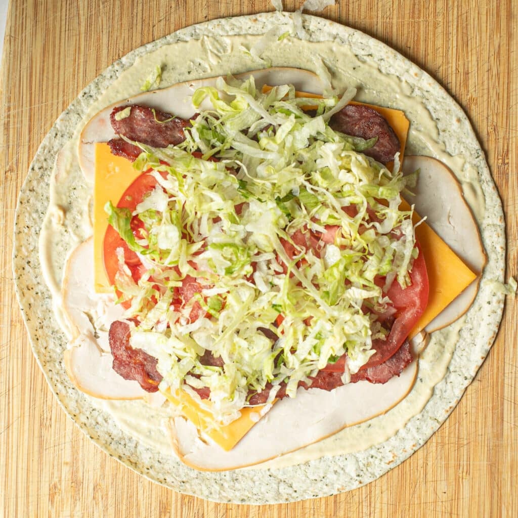 sliced turkey, cheese, tomatoes, bacon and shredded lettuce on a flour tortilla