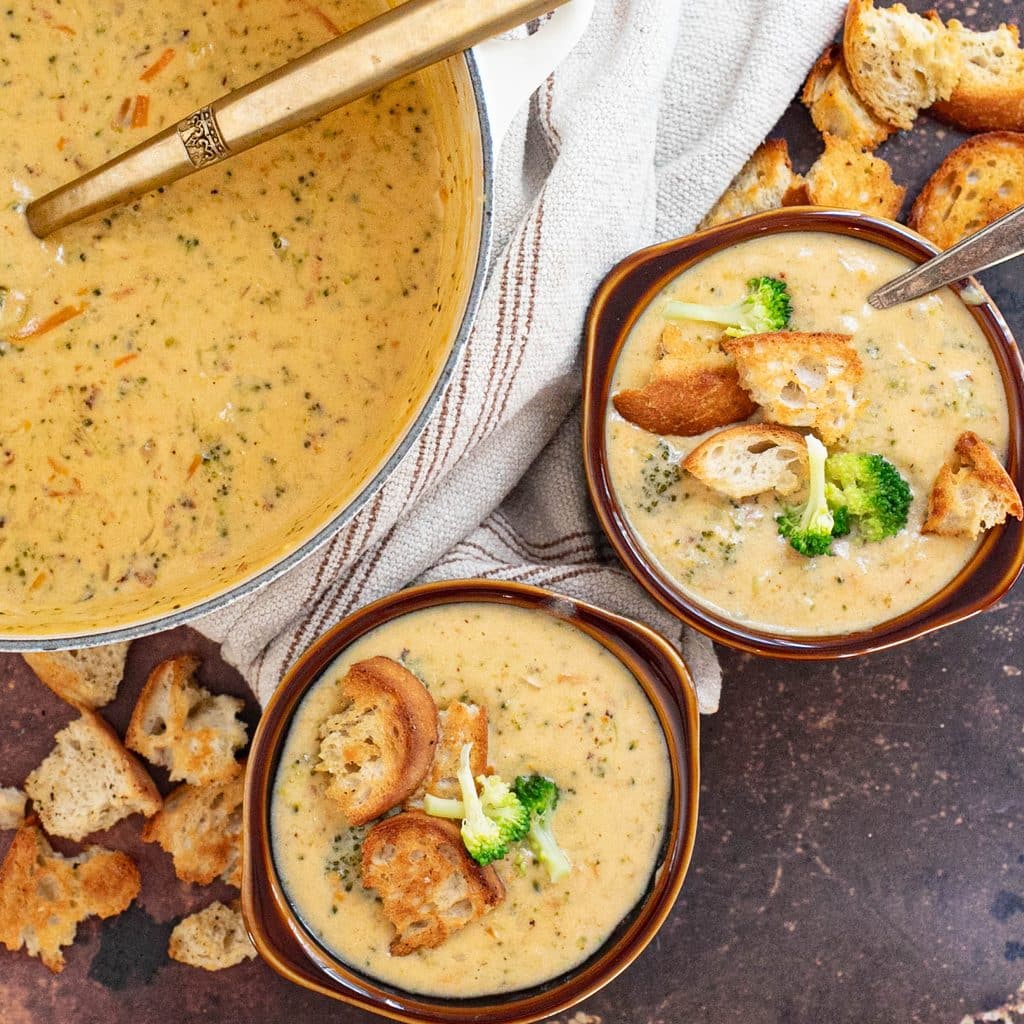 two bowls of broccoli cheddar soup next to a stock pot of soup