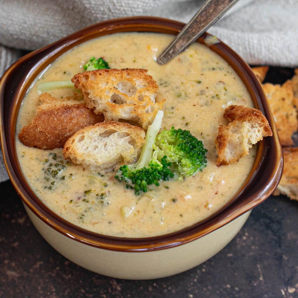a crock of broccoli cheddar soup topped with sourdough croutons