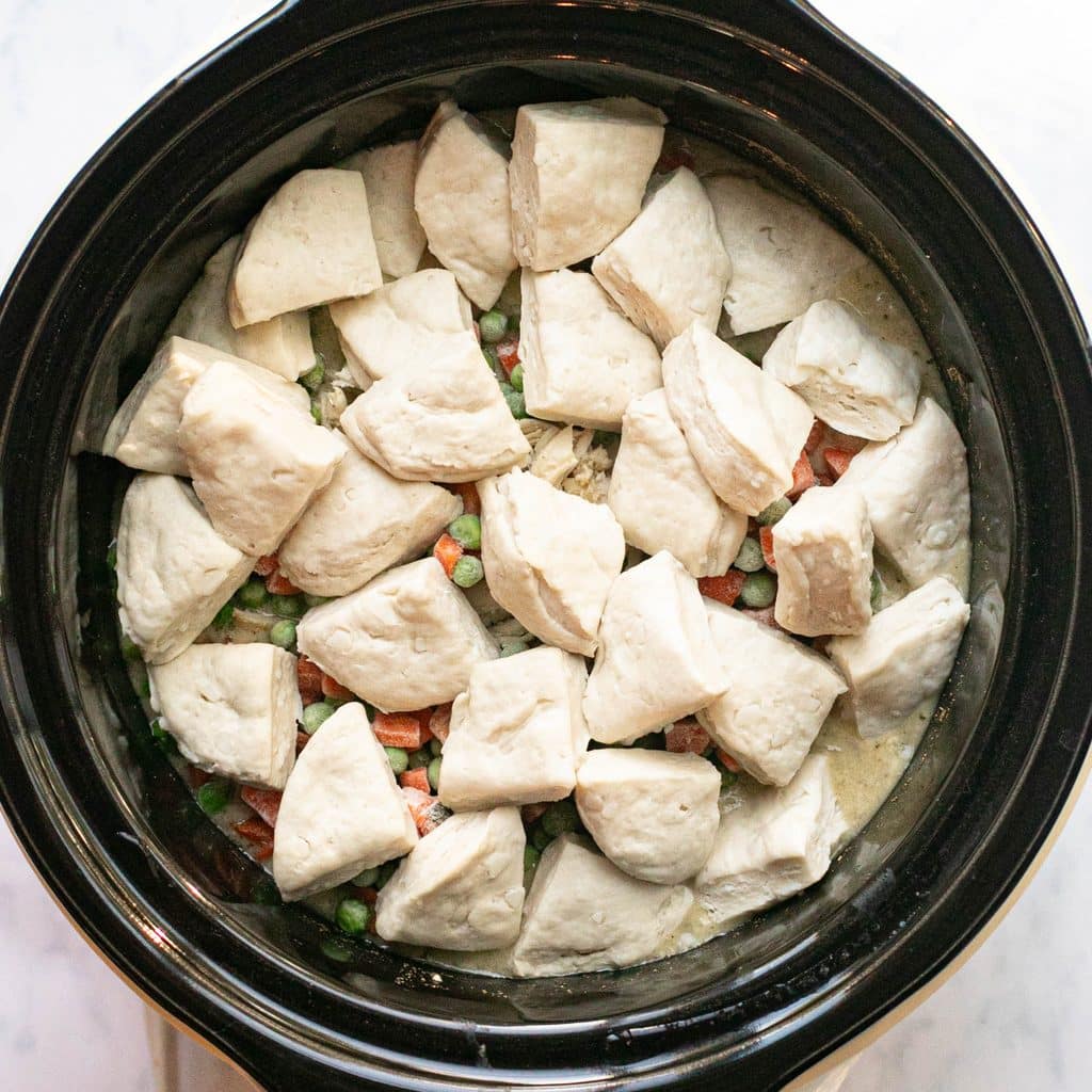 quartered biscuits arranged over frozen vegetables in a crockpot