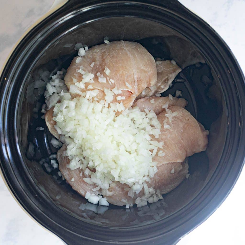 chicken breasts and chopped onions in a crockpot