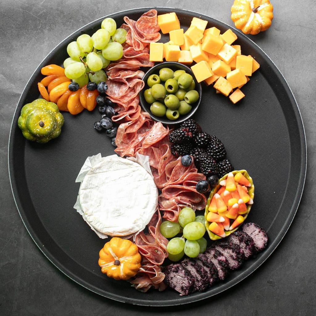 salami, cheeses, olives, candy corn and dried fruit on a round black serving board