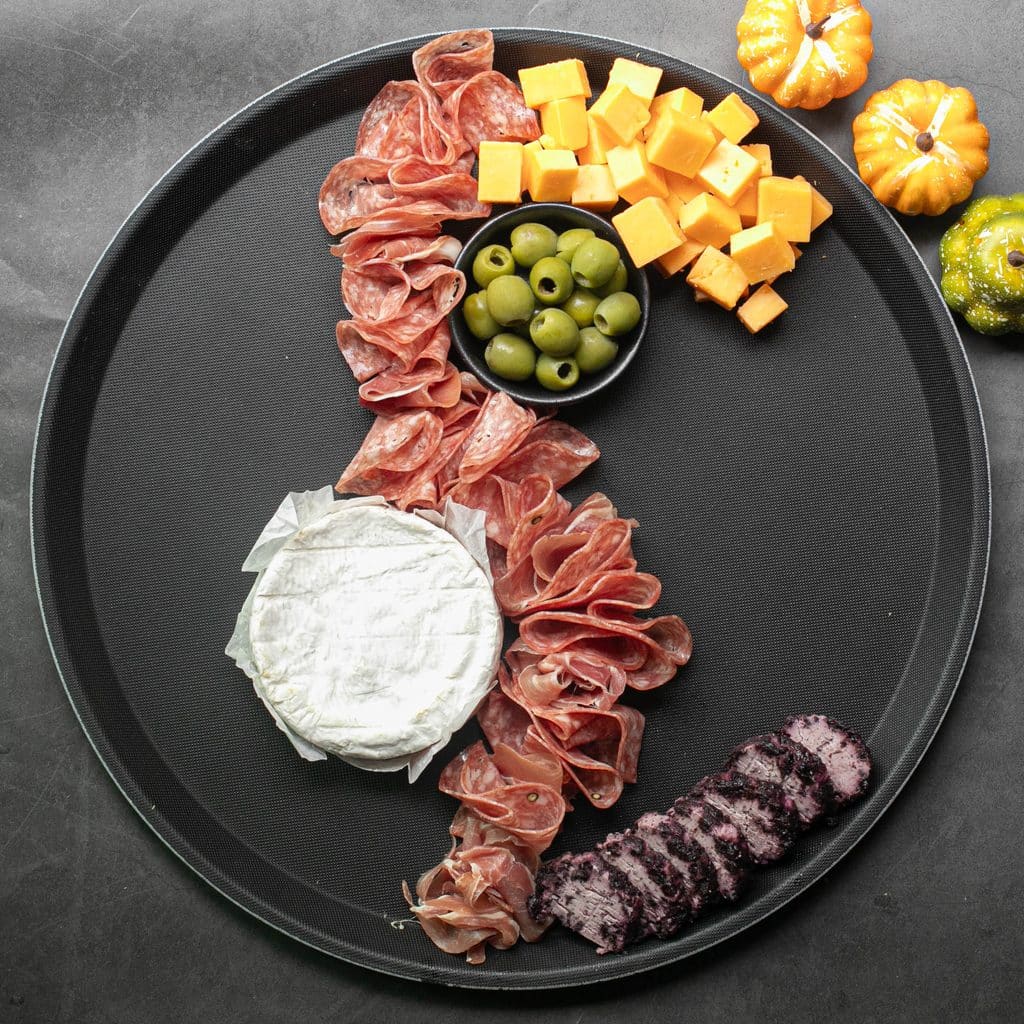 salami, cheeses and green olives on a round black serving tray
