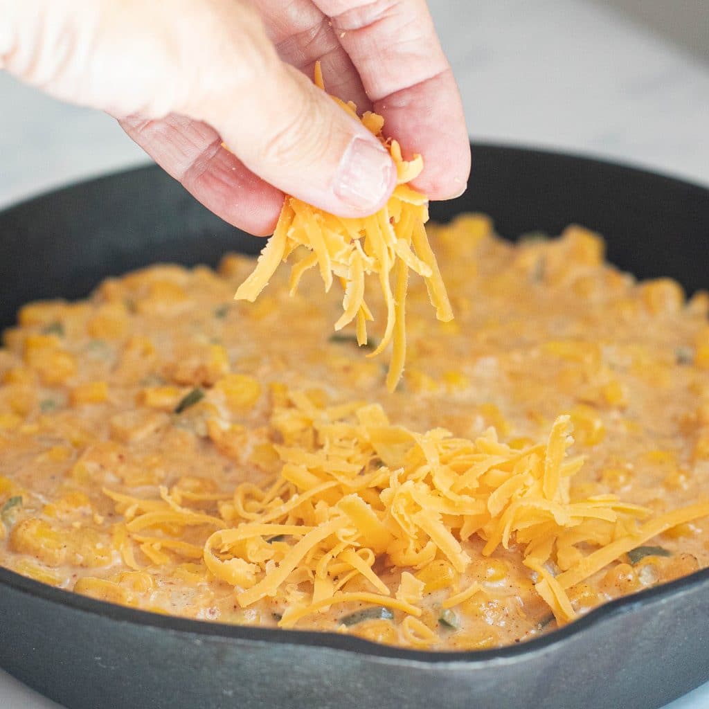 shredded cheddar cheese being sprinkled on top of corn dip
