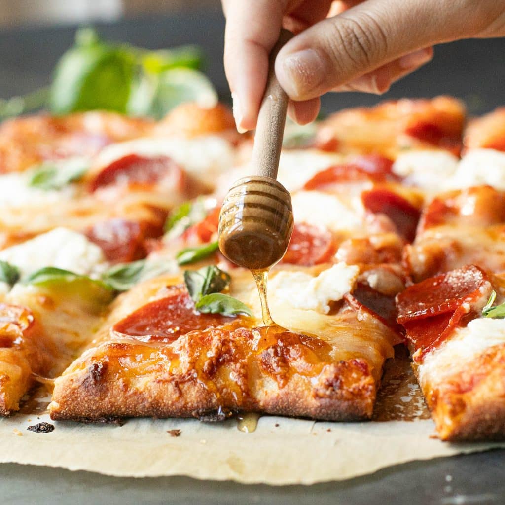 a honey wand drizzling honey onto a slice of pizza