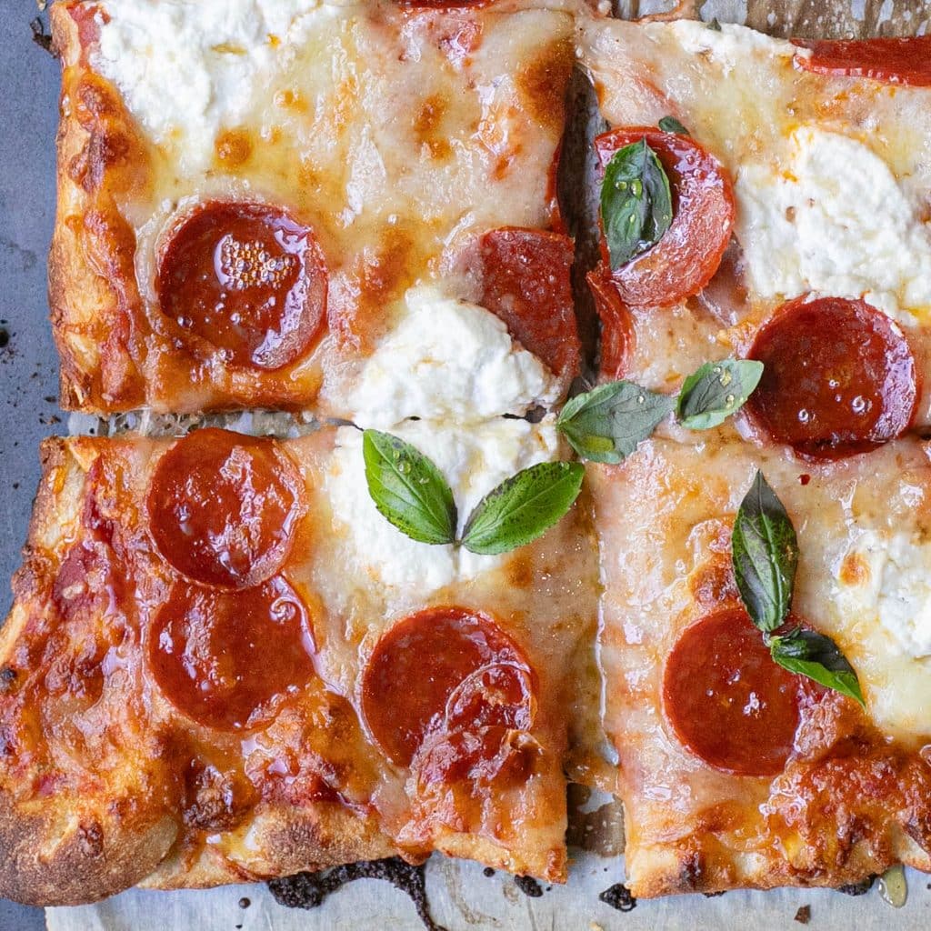 squares of hot honey pepperoni pizza with ricotta cheese and basil
