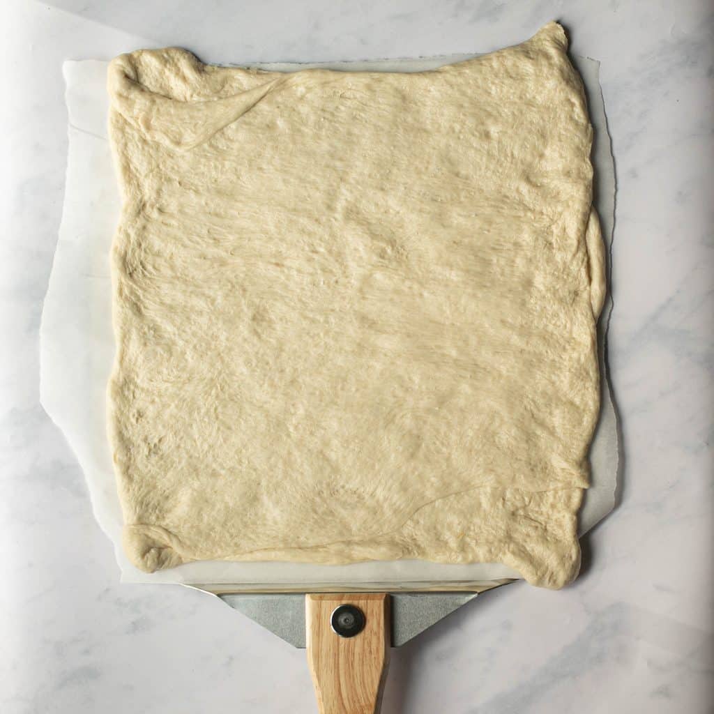 pizza dough stretched into a square shape on a pizza peel