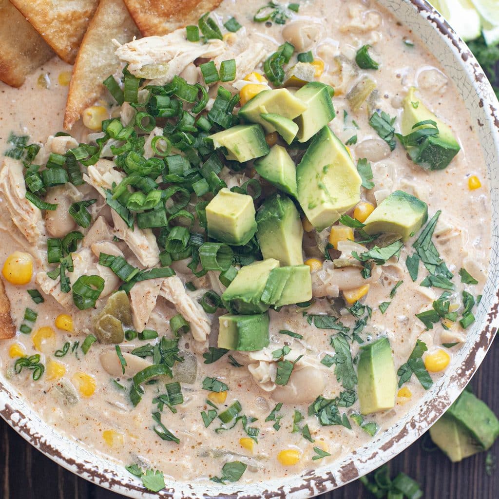white chicken chili topped with chopped scallions and avocados