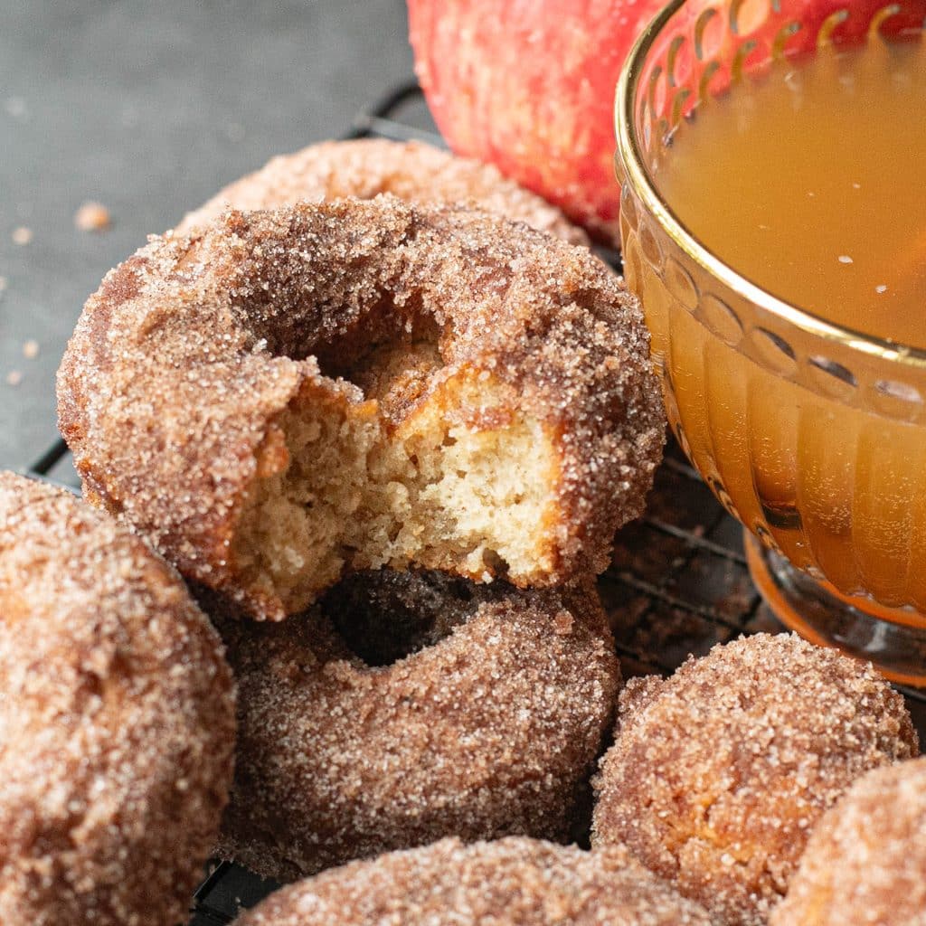 a half eaten apple cider donut next to a mug of apple cider