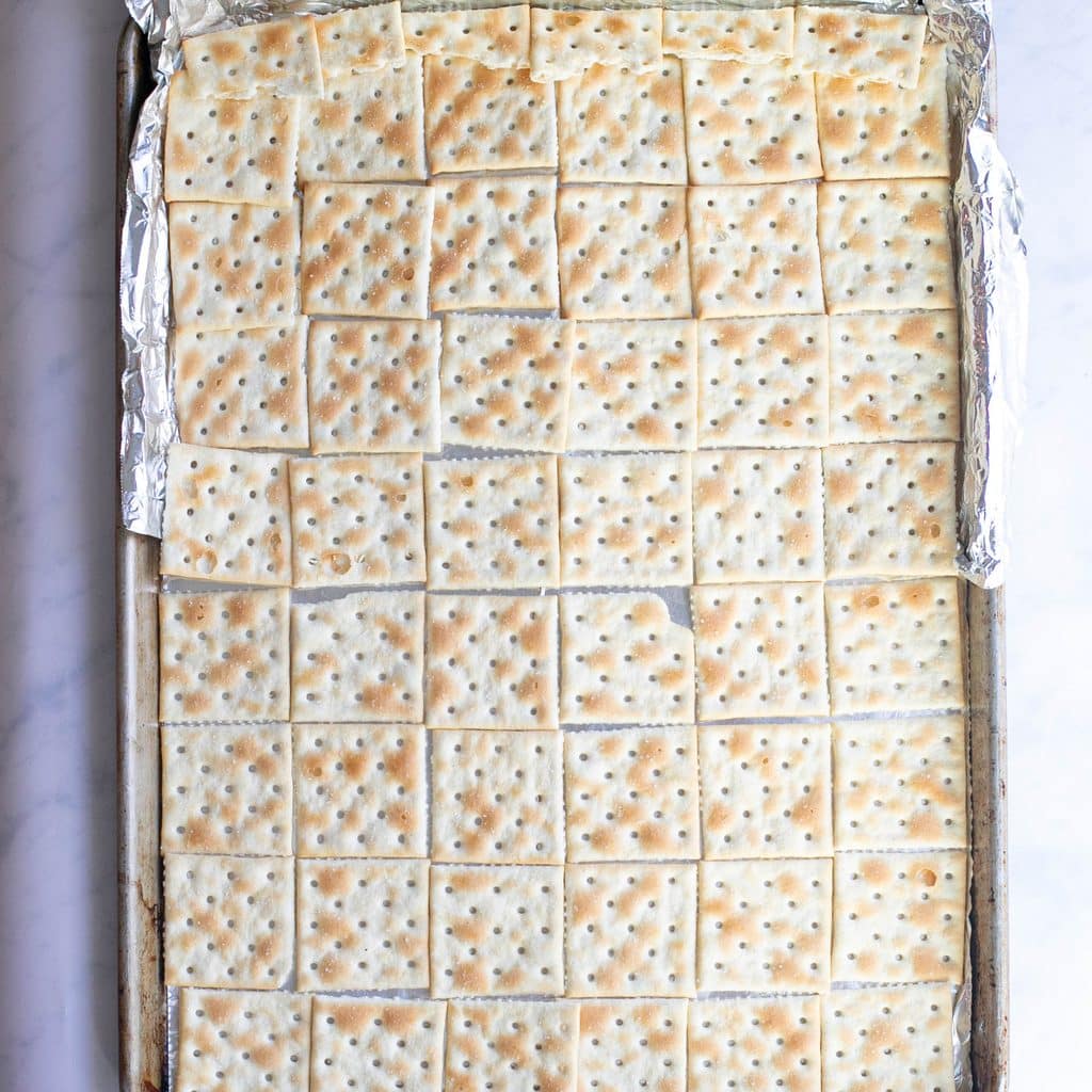 saltine crackers arranged in rows on a baking sheet