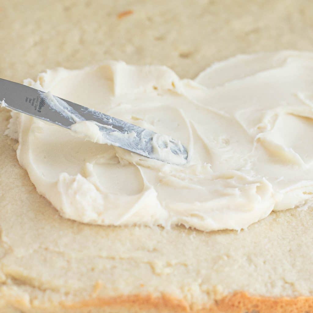 a spatula spreading frosting onto a cookie layer