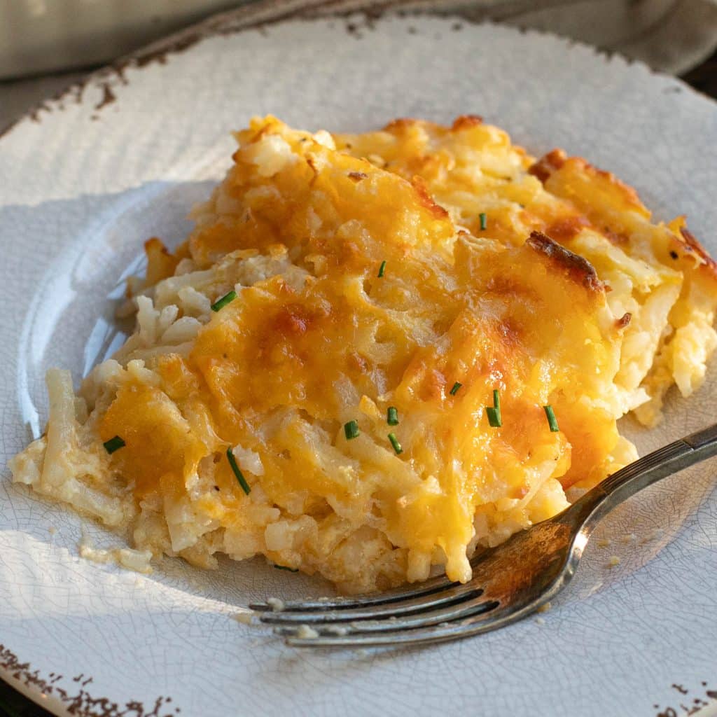 a serving of Cracker Barrel hashbrown casserole on a white plate with a silver fork