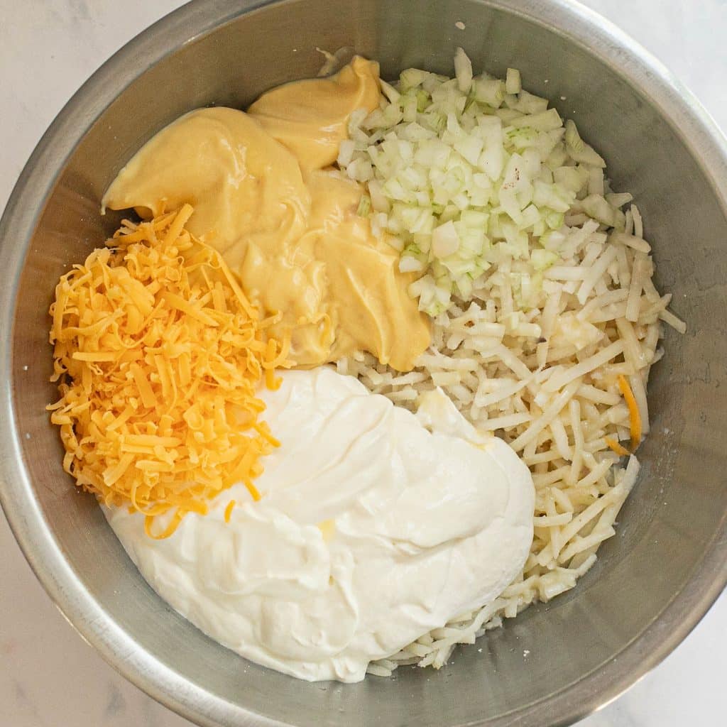 shredded potatoes in a bowl with grated cheddar cheese, diced onions, cream of chicken soup and sour cream