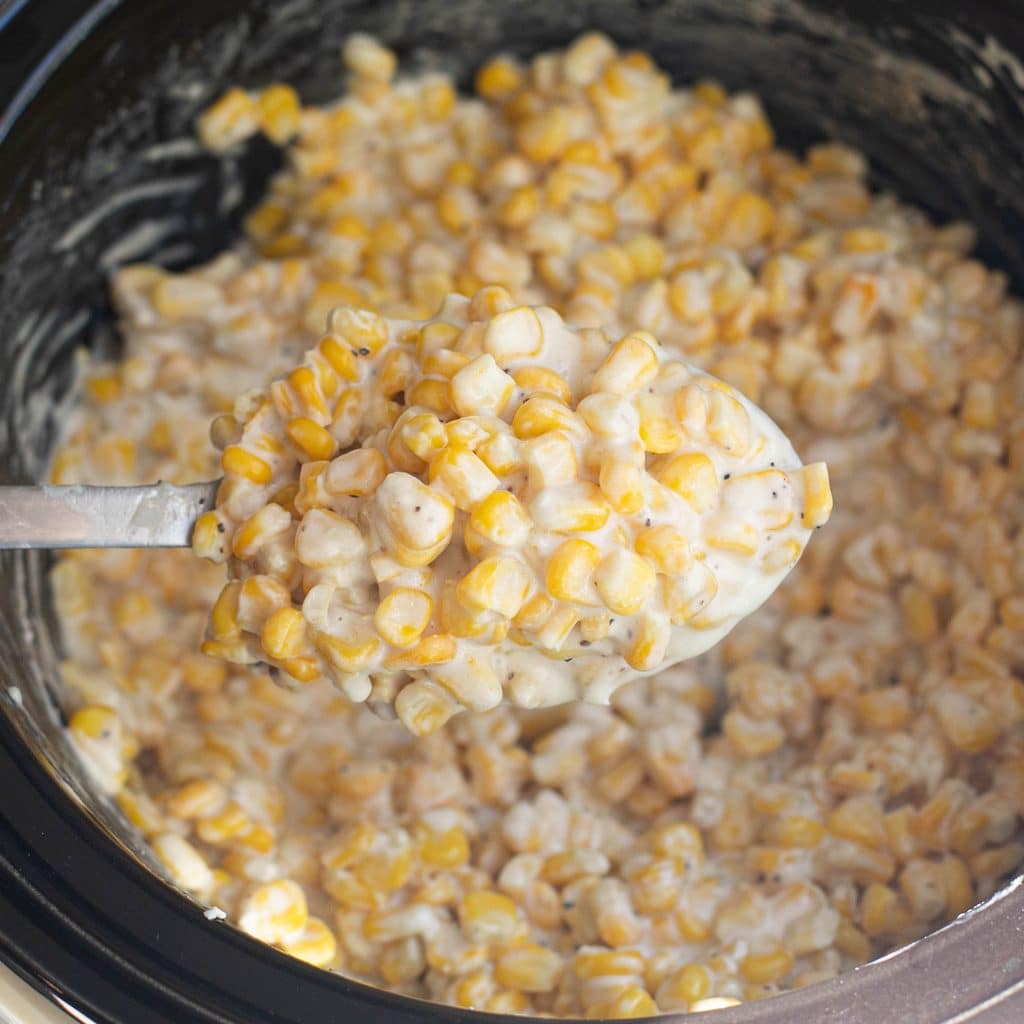 a large serving spoon holding slow cooker creamed corn