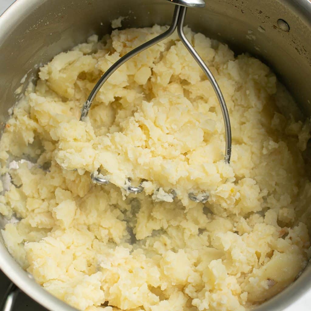a potato masher mashing potatoes in a pot