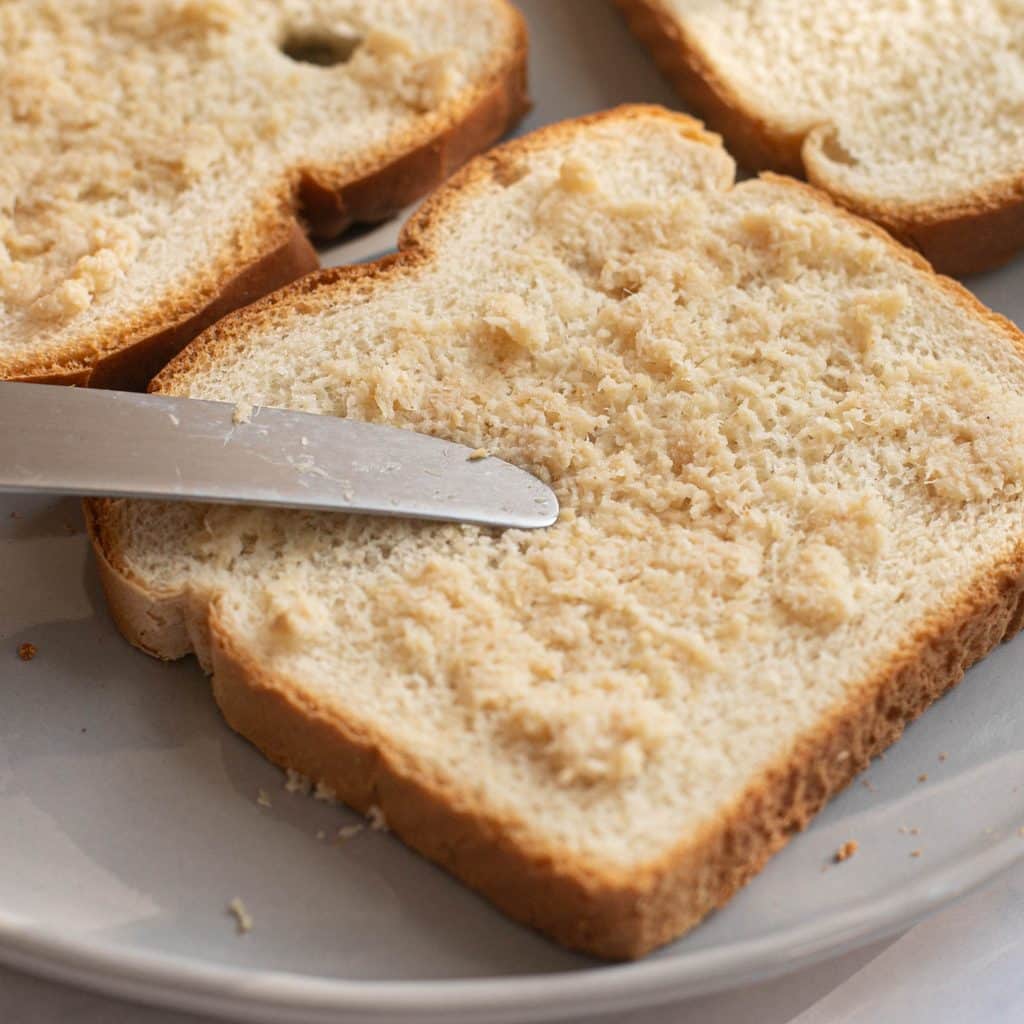 a knife spreading horseradish onto a piece of white bread