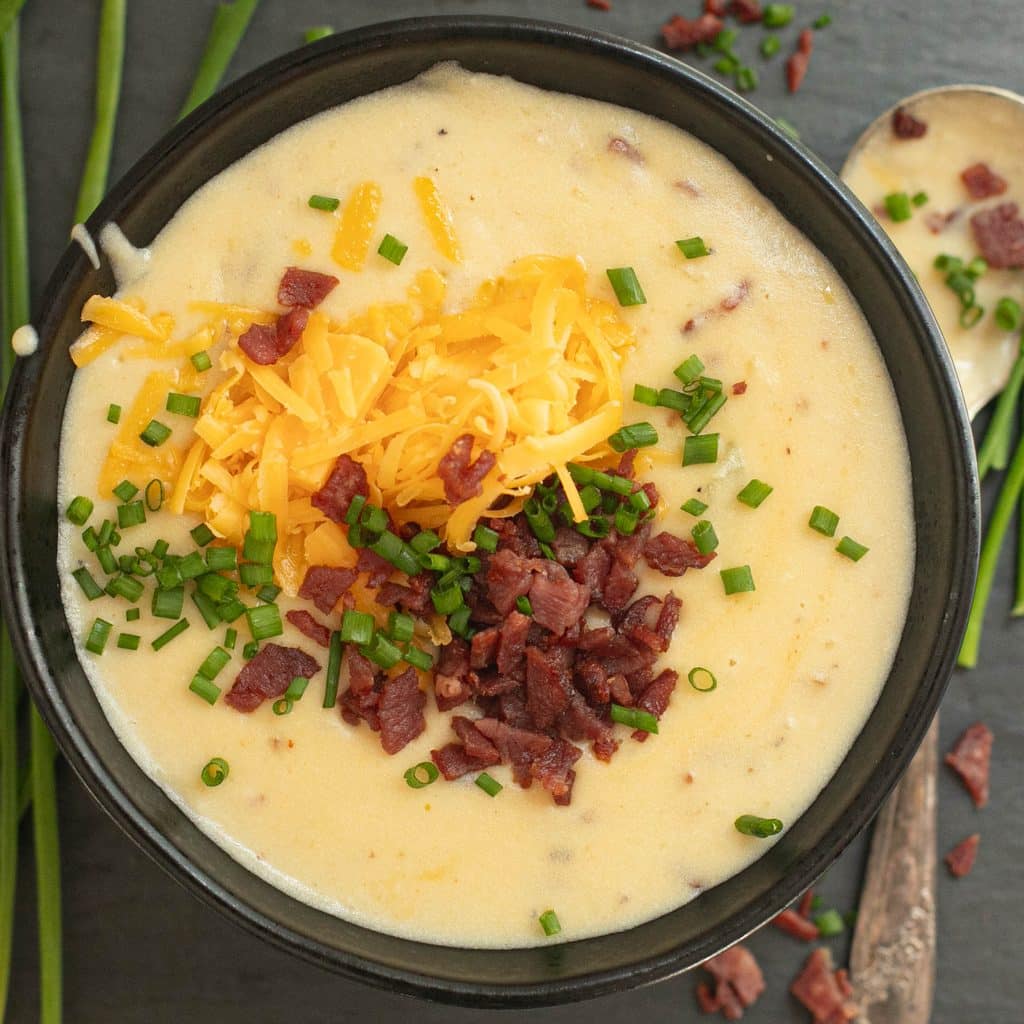 loaded baked potato soup in a black bowl topped with bacon bits and grated cheese