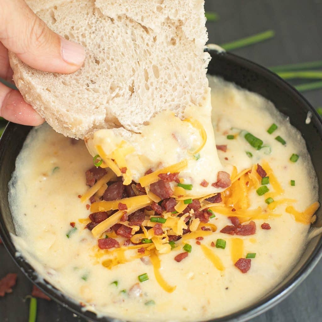 a piece of bread being dipped into loaded baked potato soup