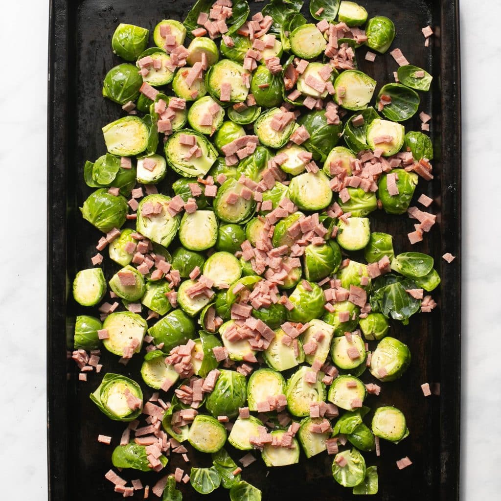 Brussels sprouts and diced bacon spread onto a baking sheet