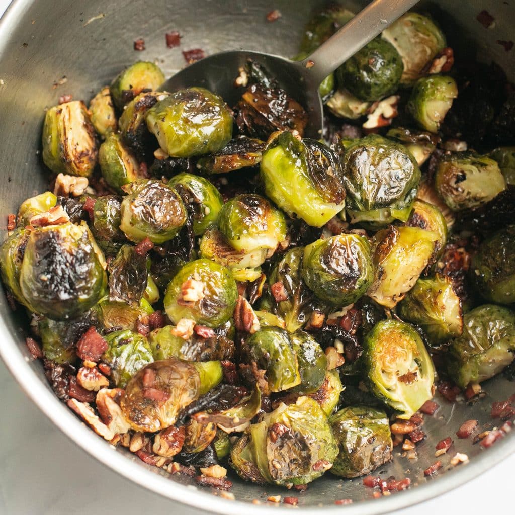 Brussels sprouts being tossed in maple syrup in a mixing bowl