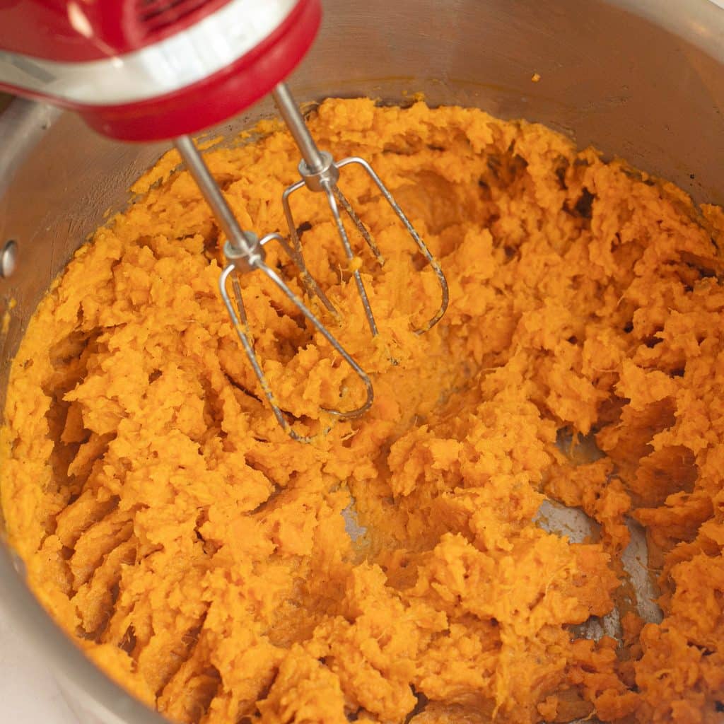 a hand mixer beating cooked sweet potatoes