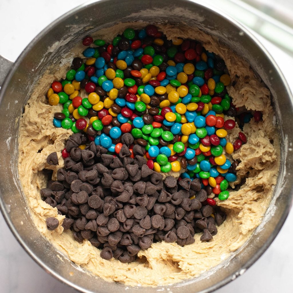 M&Ms and chocolate chips over cookie batter in a mixing bowl