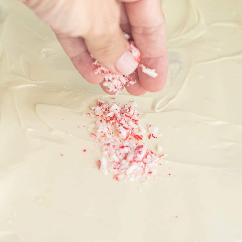 a hand sprinkling crush peppermints onto melted white chocolate