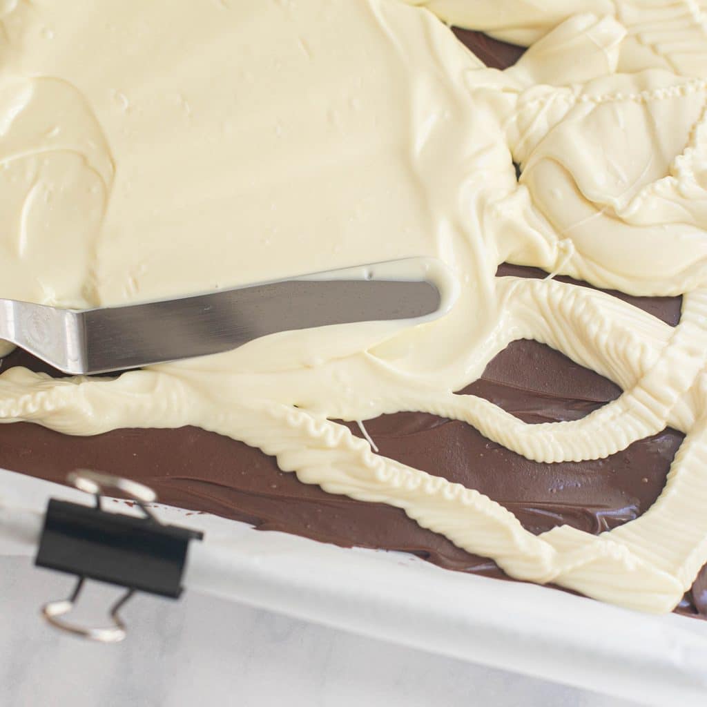 an offset spatula spreading melted white chocolate over a semisweet chocolate layer
