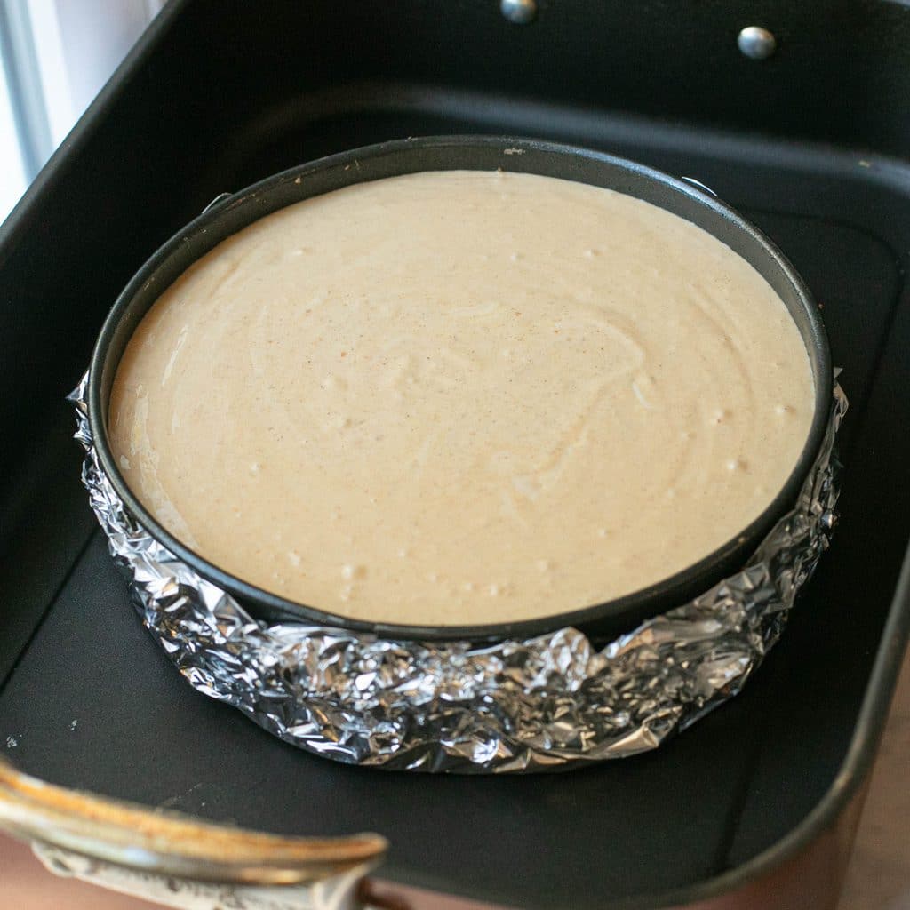 pumpkin cheesecake batter in a springform pan inside a roasting pan before baking