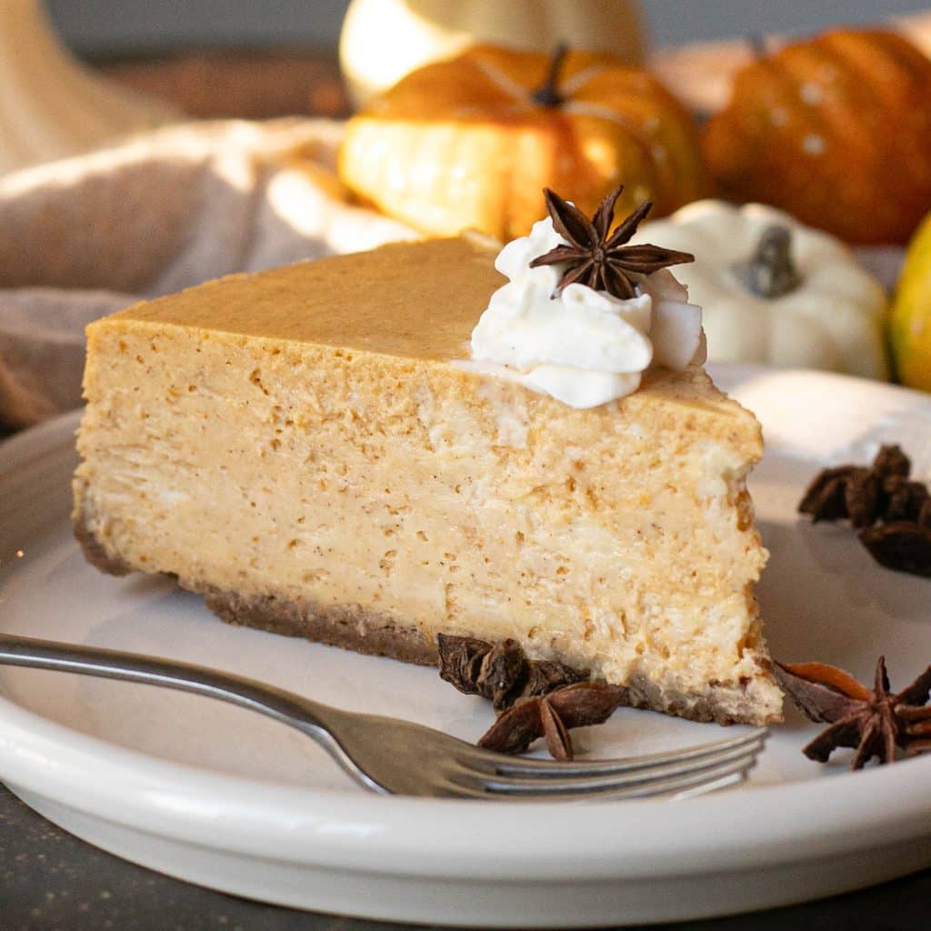 a slice of pumpkin cheesecake topped with whipped cream on a white plate
