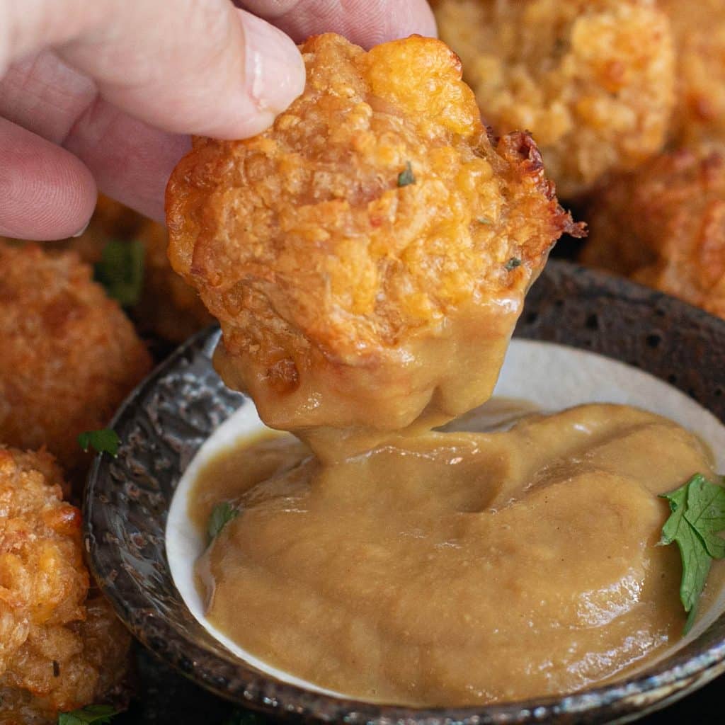 a hand dipping a Bisquick sausage ball into honey mustard
