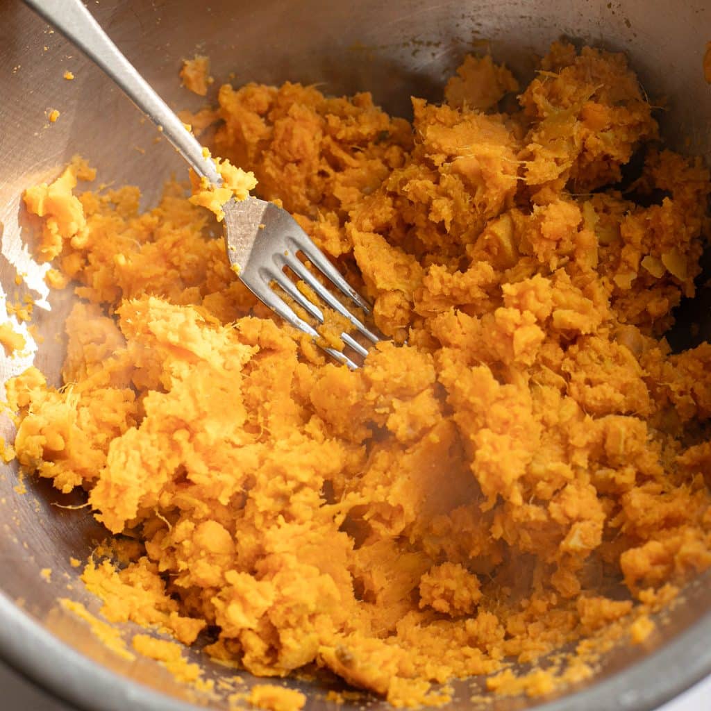 a fork mashing sweet potatoes in a bowl