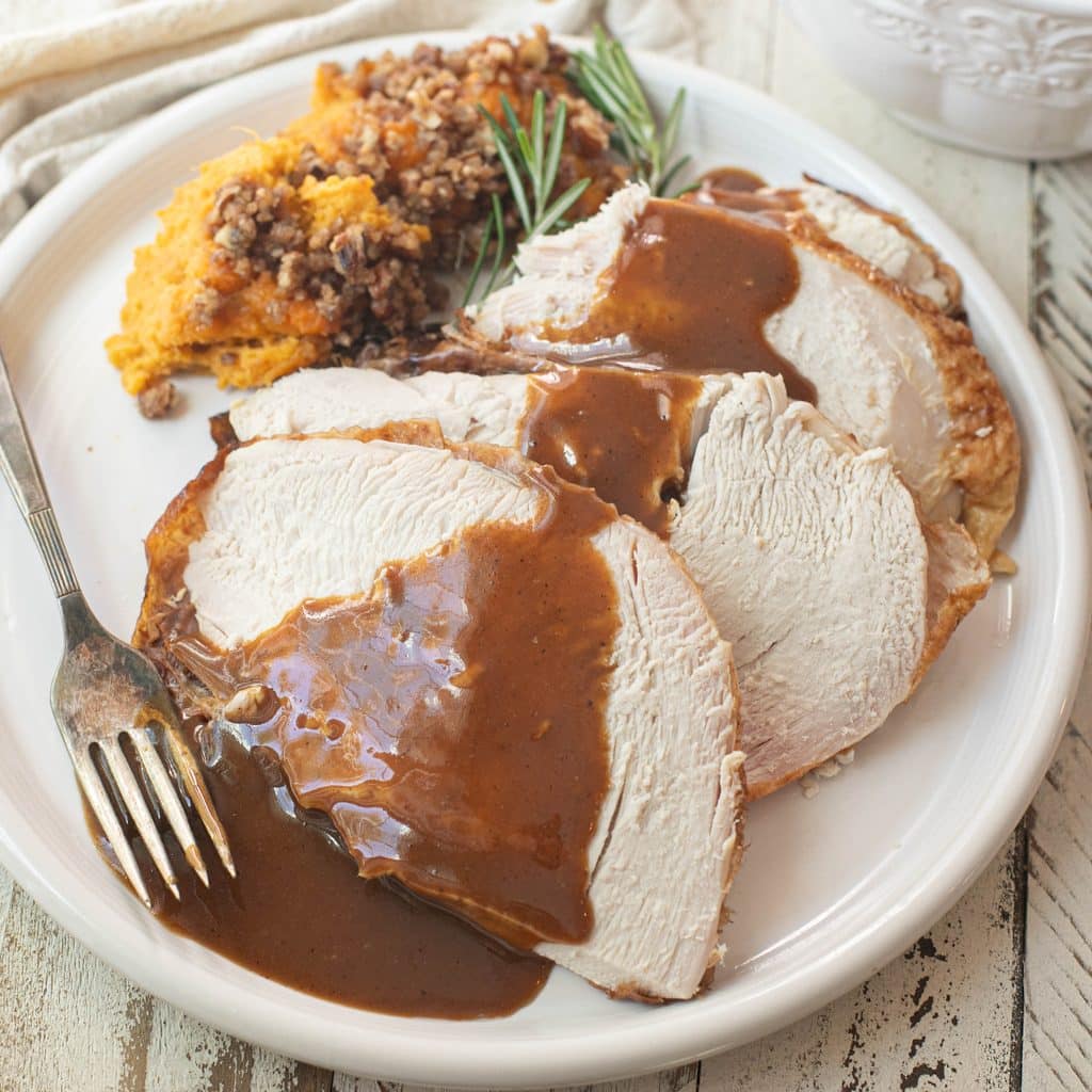 sliced  turkey on a white plate topped with homemade gravy
